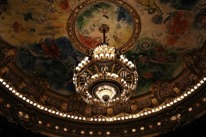 Chandelier hangs under a painted ceiling.